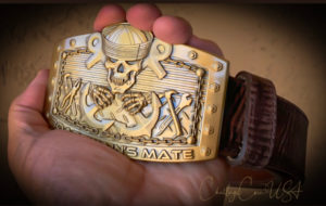 Gold-tone belt buckle featuring a Boatswain's Mate emblem with tools and rope design. Attached to a brown leather belt.