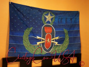 Blue flag with white stars. Features an emblem with a bomb, laurel wreath, and gold lightning bolts. EOD design.