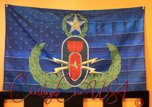 Blue flag with EOD emblem. Gold wreath surrounds a bomb and star. White stripes run horizontally. Challenge Coin USA brand.