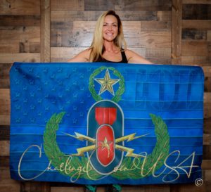 Blue EOD flag with gold emblem and star. Woman holds flag. Challenge Coin USA logo visible.