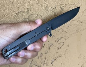 Closed Medford M48 knife. Black titanium frame with a partially visible Challenge Coin USA