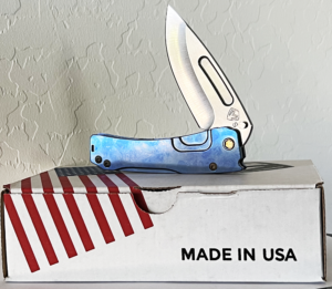 Blue and silver folding knife rests on a box with red and white stripes. The knife handle has a textured, marbled design.