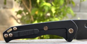 Black Medford Micro T knife. Visible hardware, including a bronze screw. Challenge Coin USA branding on the handle.