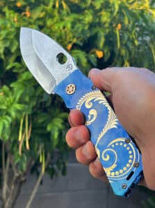 Blue Medford TFF1 folding knife with gold floral design. Silver blade, held in a hand